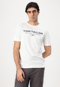 Hvid bomulds-T-shirt med korte ærmer, der har et marineblåt "TOM TAILOR" logo og tekstdesign på tværs af brystet.