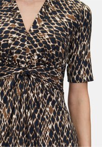 Hnědo-námořnické šaty se vzorem a krátkými rukávy, s nahrnutým detailním uzlem v pase a hlubokým výstřihem do V.
