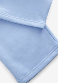 Tissu de sweatshirt bleu clair avec une texture douce, présentant des coutures visibles le long des ourlets et des bords. Le design a une coupe décontractée.