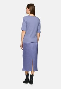 Light purple top with short sleeves paired with a mid-length skirt featuring a back split. Model wears black ankle boots.