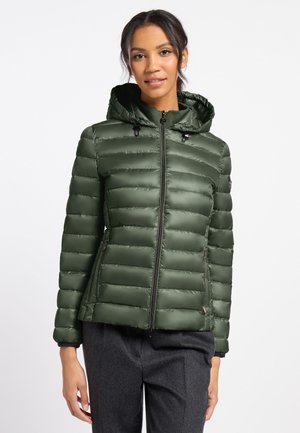 Woman wearing a dark green quilted hooded puffer jacket with a front zipper and dark gray pants against a plain background.