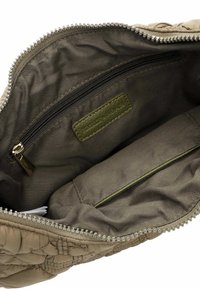 Intérieur d'un sac en tissu matelassé beige avec une doublure vert foncé, une poche zippée et un label en patch. Fermeture éclair avec de petites dents décoratives.