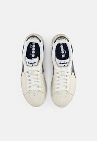 Zapatillas Diadora en cuero blanco roto con acentos en color marino. Incluyen cordones blancos, puntera perforada y logo en la lengüeta.