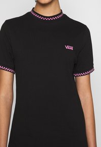 T-shirt noir à manches courtes avec des accents en damier rose sur le col et les poignets, et un petit logo Vans rose sur la poitrine.