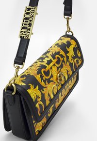 Czarna torebka ze złotym wzorem, z przednią klapką, złotymi elementami i odpinanym paskiem. Charakteryzuje się misternymi barokowymi zdobieniami.