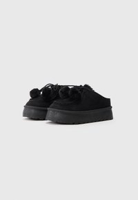 Chaussures à plateforme en daim noir avec un bout rond, ornées de trois pompons duveteux et d'un design cousu, présentant une semelle en caoutchouc texturé.
