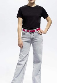 Schwarzes Baumwoll-T-Shirt kombiniert mit hellgrauen weiten Jeans und einem fuchsiafarbenen Gürtel. Der Gürtel hat eine runde silberne Schnalle.