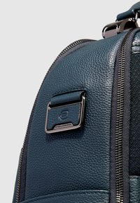 Zaino in pelle blu con finitura testurizzata, caratterizzato da una cerniera argentata e da una toppa rettangolare con il logo sul lato.