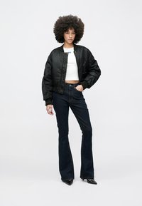 Musta bomber-takki, jossa on lyhyt malli, päällä valkoinen crop-top, yhdistetty liehuviin tummansinisiin farkkuihin ja mustiin terävälestisiin korkokenkiin.