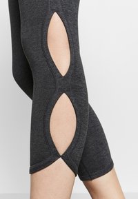 Svarta leggings med utskärningar på sidorna. Tillverkade av ett elastiskt material, med detaljerad sömnad längs kanterna och en medellång design.