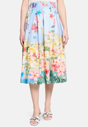 Jupe midi bleu clair avec des motifs colorés de ville balnéaire, fleurs, créatures marines et récif corallien, portée avec des sandales blanches à bout ouvert.