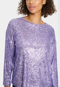 Purple sequined sweater featuring a round neck and three-quarter sleeves with a textured, shiny surface and a loose fit.