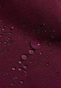 Bordowy materiał o gładkiej fakturze, zgrupowany w krople wody różnej wielkości, podkreślający jego właściwości wodoodporne.