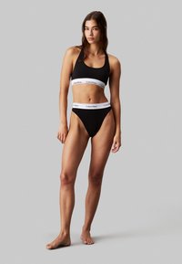 Fekete sportmelltartó és bikini szett Calvin Klein logóval fehér színben, varratnélküli kivitelben és puha anyagból. Magas szabású lábazatok a bikinin.