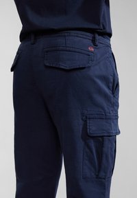 Navy cargo pants made of lightweight fabric, featuring side pockets, back patch pockets, and reinforced stitching on seams.