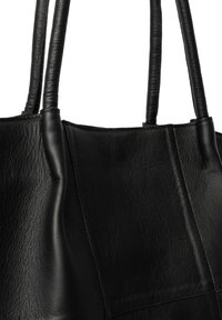 Zwarte leren tote bag met een gladde textuur, stevige buitennaadtoes en dubbele lange hengsels voor het dragen.