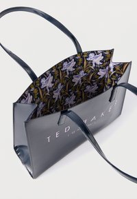 Τσάντα tote από συνθετικό δέρμα σε ναυτικό μπλε χρώμα με εσωτερικό διακοσμημένο με ανθικό μοτίβο, επιδεικνύει εμφανές λογότυπο, δύο λαβές και καλοσχηματισμένο σχέδιο.