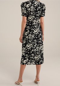 Černé květinové šaty s přiléhavým střihem, nabíranými rukávy a délkou ke kolenům. Bílý květinový vzor s texturovaným detailem látky.
