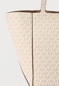Torba tote iz kremenasto belega prevlečenega platna z vtisnjenim vzorcem logotipa v kaki barvi, rjavo usnjeno obrobo, širokim odprtim vrhom in dvojno ramensko naramnico.