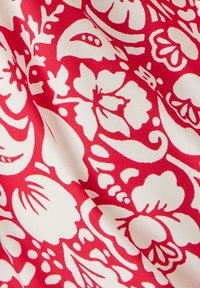 Tessuto rosso con intricati motivi floreali bianchi, caratterizzato da varie forme come petali e foglie, creando un design vivace e texturizzato.