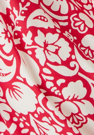 Tissu rouge avec des motifs floraux blancs complexes, comportant diverses formes comme des pétales et des feuilles, créant un design vibrant et texturé.