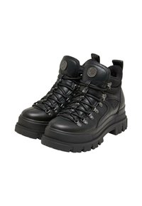 Paire de chaussures de randonnée en cuir noir à lacets avec semelles épaisses à crampons et logo métallique rond sur des languettes matelassées.