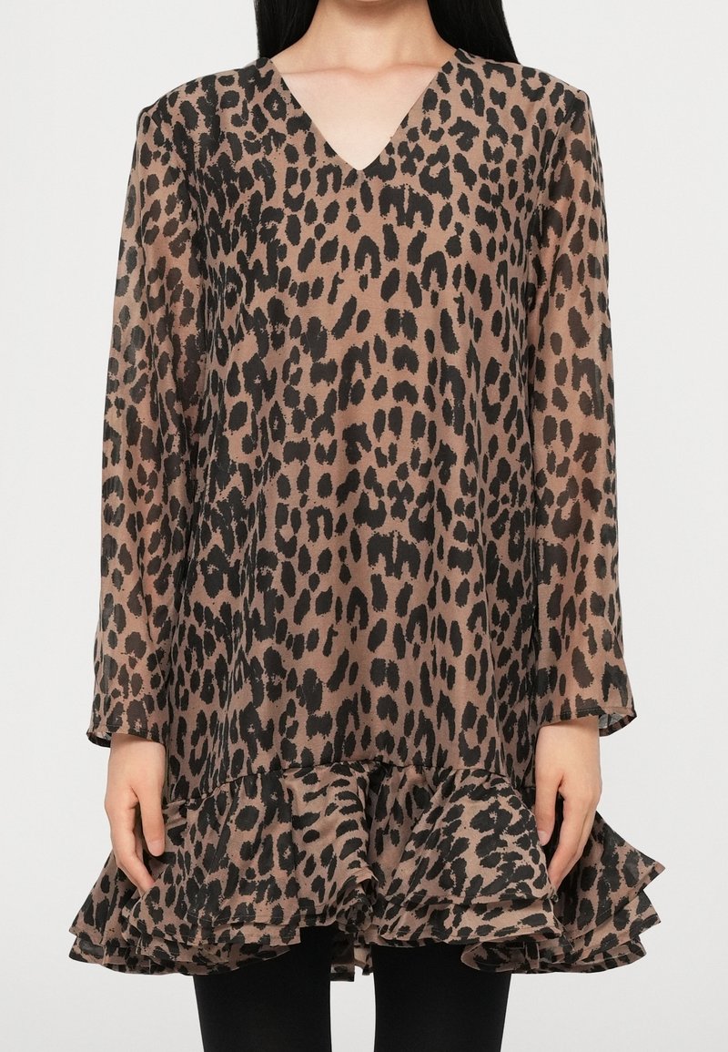 Femme portant une robe marron à manches longues imprimée léopard avec un col en V et un ourlet à volants, associée à un legging noir.