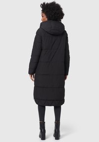 Abrigo de plumas negro con capucha, con un diseño acolchado y mangas largas, combinado con jeans negros ajustados y botas de tobillo.