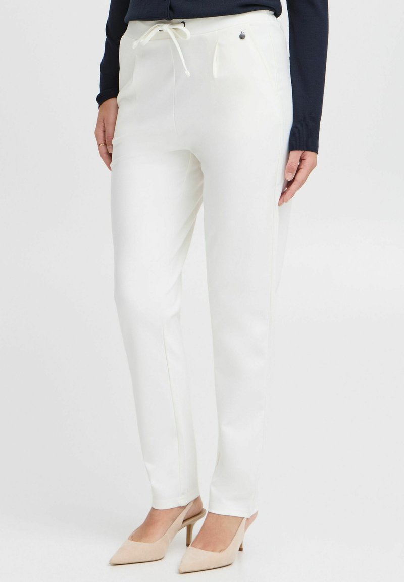 Pantalon blanc avec taille élastique à cordon, plis avant, poches latérales et texture lisse. Associé à des chaussures à talons beiges.