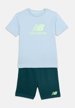 Vaaleansininen lyhythihainen New Balancen paita, jossa logo, ja tummanvihreät shortsit, joissa New Balancen logo vasemmassa lahkeessa.