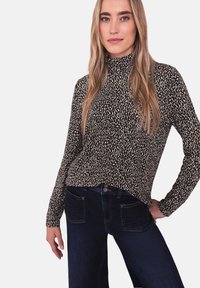 Pull à col roulé à motif noir et blanc avec manches longues, associé à un jean en denim bleu foncé avec poches et détails de coutures.