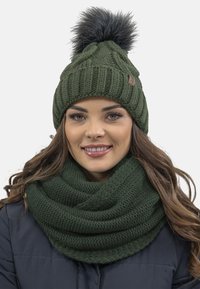 Strikket grøn beanie med struktureret mønster og mørk pom-pom, parret med en tyk, matchende grøn cowl-scarf. Begge er lavet af blødt garn.
