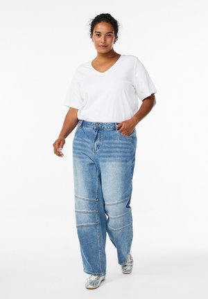 Lightweight white V-neck top paired with loose denim jeans featuring a faded finish and panel stitching. Model wearing metallic sneakers.