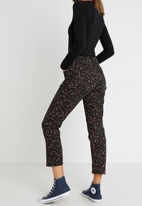 Pantalones negros texturizados con un colorido patrón floral, con una cintura ajustada y un corte cropped, combinados con zapatillas altas azules.