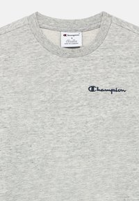 Ανοιχτό γκρι βαμβακερό μπλουζάκι με στρογγυλή λαιμόκοψη, με μπλε σκούρο κεντητό λογότυπο "Champion" στο αριστερό στήθος.