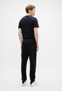 Μαύρο βαμβακερό t-shirt και ασορτί παντελόνια φόρμας, με χαλαρή γραμμή, ελαστική μέση και λευκά αθλητικά παπούτσια. Λείο υφή, μίνιμαλ σχέδιο.