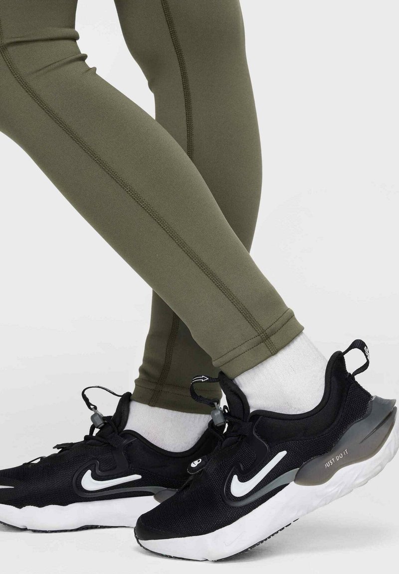 Scarpe da ginnastica nere con dettagli bianchi, abbinate a leggings verde oliva con una texture liscia e dettagli di cucitura a contrasto.