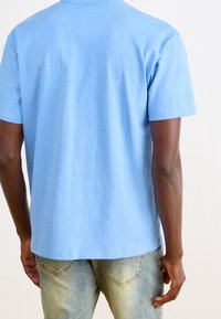 Ljusblå bomull T-shirt med rund hals, korta ärmar och rak nederkant. Bärs med blekta blå denimjeans.