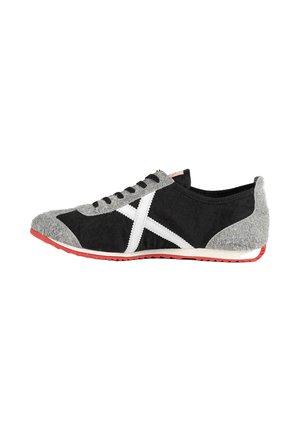 Zapatilla baja con tejido negro y gris, diseño blanco en forma de X en el lateral, cordones negros y suela roja, mostrada de perfil derecho.