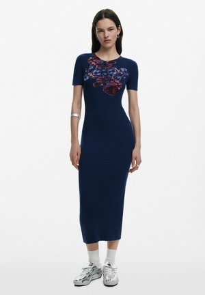 Navy ribbed knit dress with short sleeves, fitted silhouette, floral design in red and purple at chest, worn with silver sneakers.