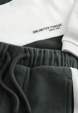 Graue und weiße Sportbekleidung mit einem strukturierten Stoff, elastischem Bund und dem Aufdruck "UNLIMITED FUNDAY SINCE 1982".