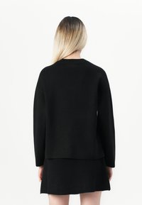 Svart strikkegenser med lange ermer, rund hals og avslappet passform, paret med et matchende svart skjørt, minimalistisk design.