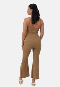 Mono de canalé marrón con tirantes finos, cuerpo ajustado, piernas acampanadas y aberturas laterales, combinado con tacones de color claro.
