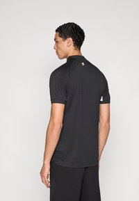 Μαύρο πόλο πουκάμισο με γιακά, κοντά μανίκια και διακριτική λεπτομέρεια λογότυπου στο πίσω μέρος. Λείο, ελαφρύ ύφασμα με εφαρμοστή σχεδίαση.