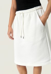 Gonna bianca in cotone con vita elastica e cordoncino. Presenta una tasca laterale e un logo ricamato discreto sulla parte anteriore.