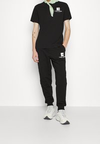 Svart t-shirt och joggers, båda med vita logotypdetaljer. T-shirten har korta ärmar, medan joggers har en figurnära design och fickor.