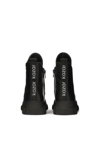 Black ankle boots with a smooth finish, featuring back zippers and prominent white branding on the sides. Thick textured soles.
