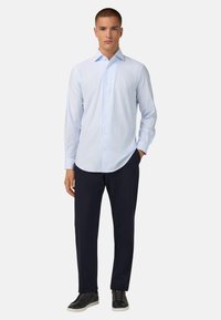 Jasnoniebieska, w paski, koszula z guzikami z materiału o gładkiej strukturze, noszona z ciemnoniebieskimi spodniami i czarnymi sneakersami.