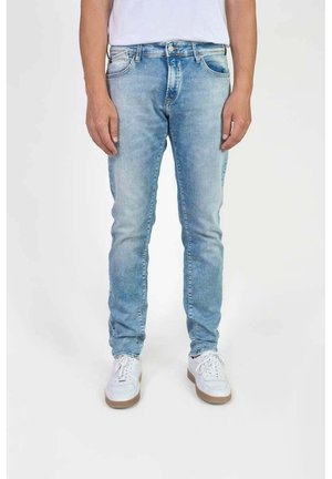 Jeans en denim bleu clair à coupe slim, avec des poches avant, une fermeture éclair et un léger effet délavé. Associés à des baskets blanches.
