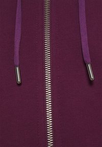 Lila zip-up hoodie med metallisk dragkedja och matchande dragsnören. Tyget är texturerat och ger ett mysigt intryck.